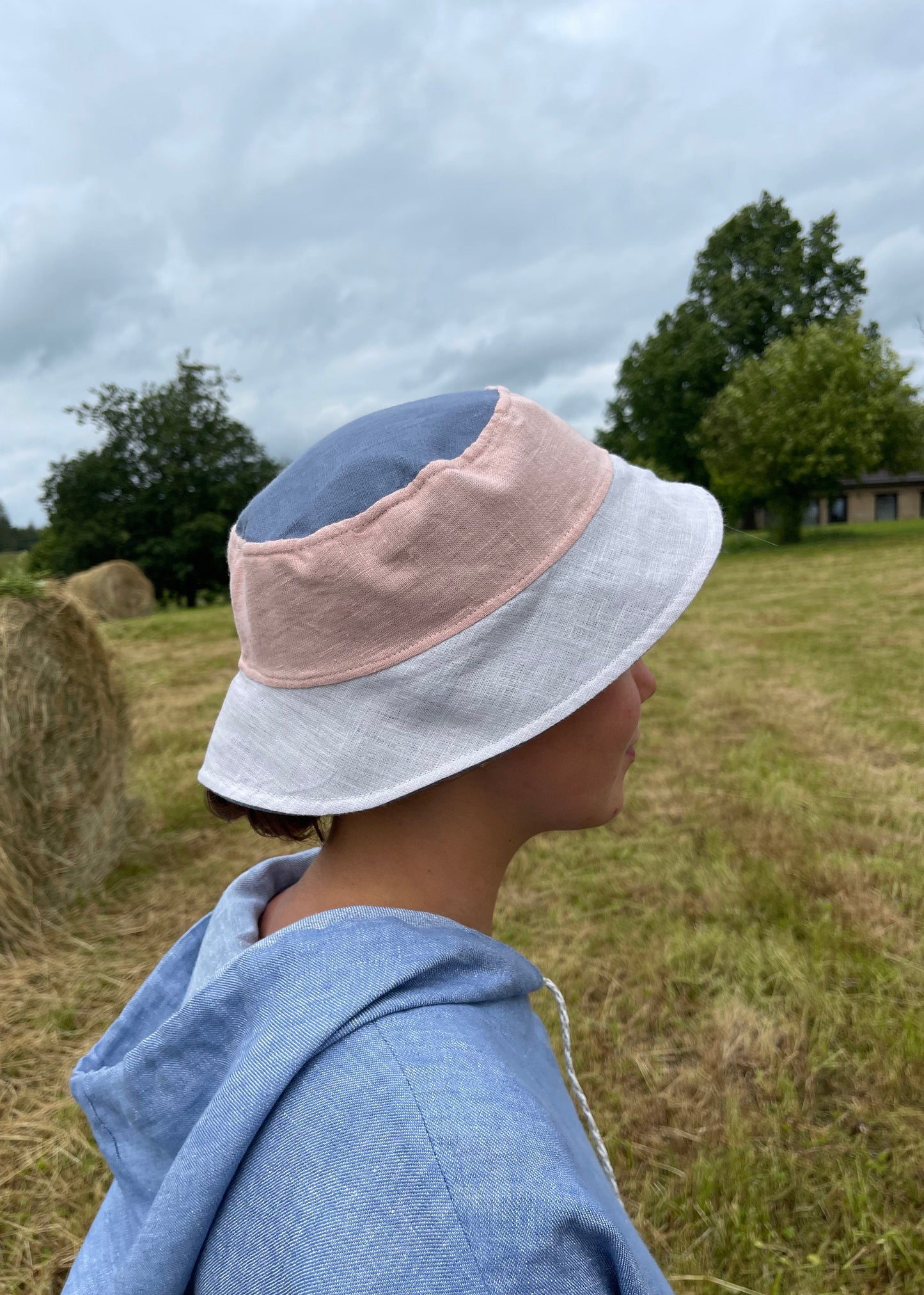 Person wearing a blue hoodie and hat standing in a field with hay bales.