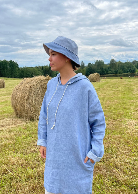 Person wearing a blue hoodie and hat standing in a field with hay bales.